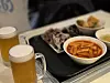 Tteokbokki (spicy rice cakes) served with fried side dishes and sundae (Korean blood sausage) next to draft beers [JIN EUN-SOO]