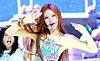 A female pop performer in a yellow top sings onstage with hand gestures during a colorful showcase.
